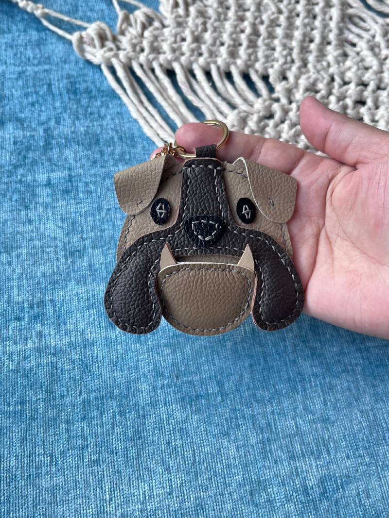 Close-up of a boutique leather bulldog charm with contrasting white stitching and brown jowls.