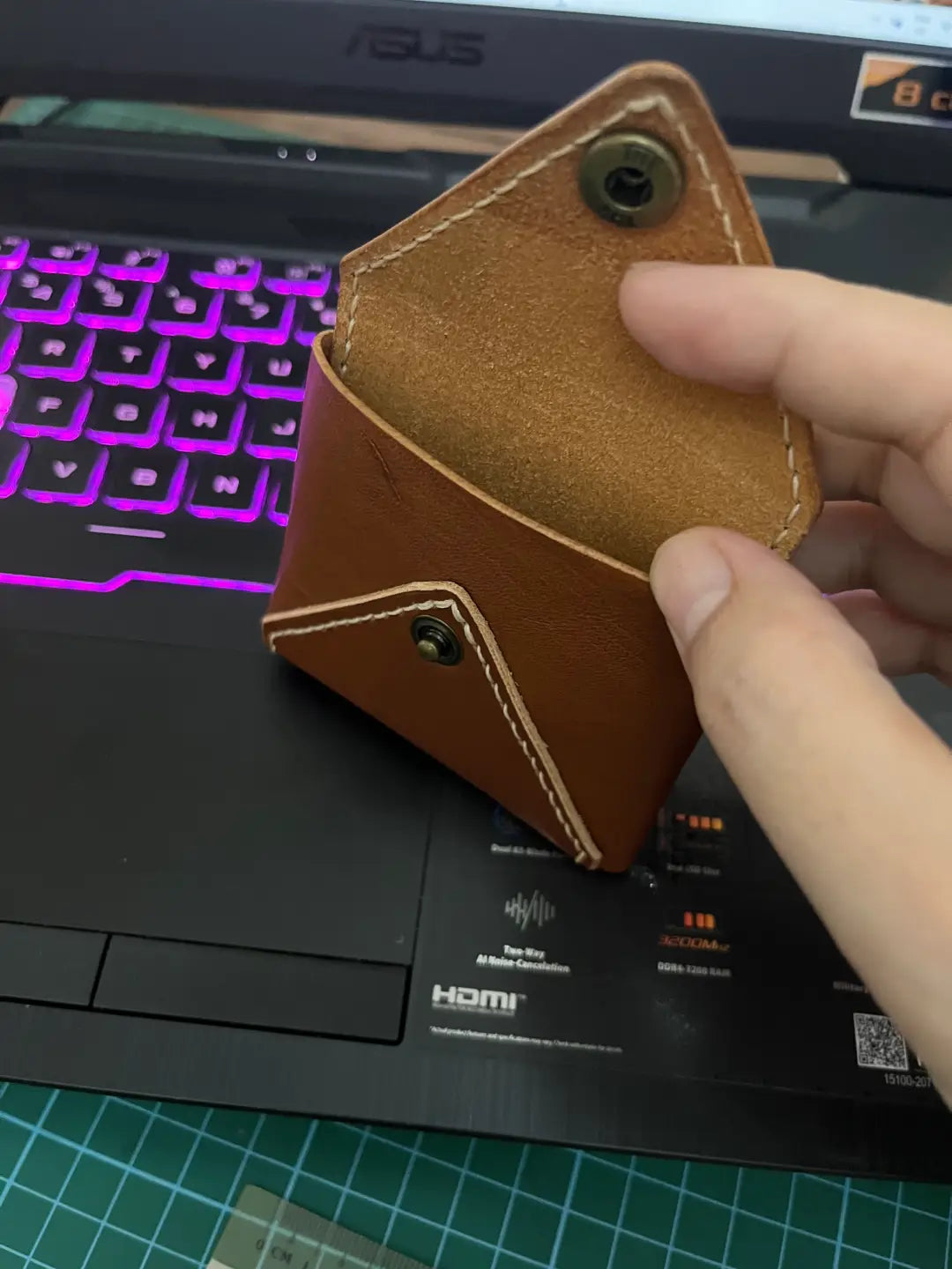 DIY brown leather coin pouch held by a hand in front of a laptop.