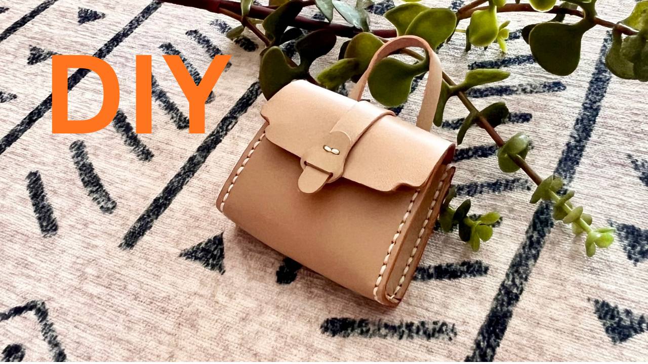 DIY tiny leather beige bag charm on a patterned surface with green leaves.