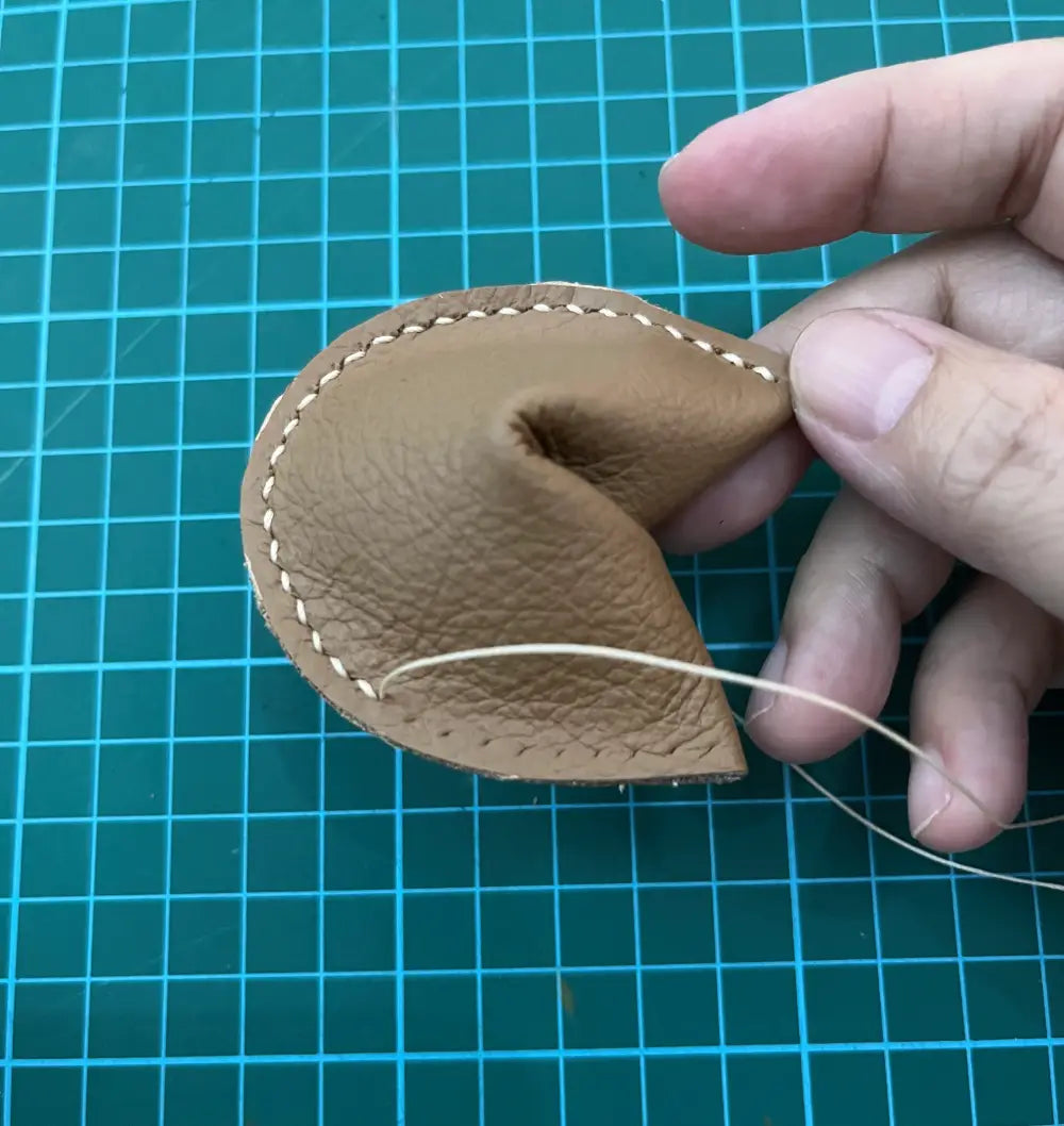 hand sewing of leather fortune cookie keychain.