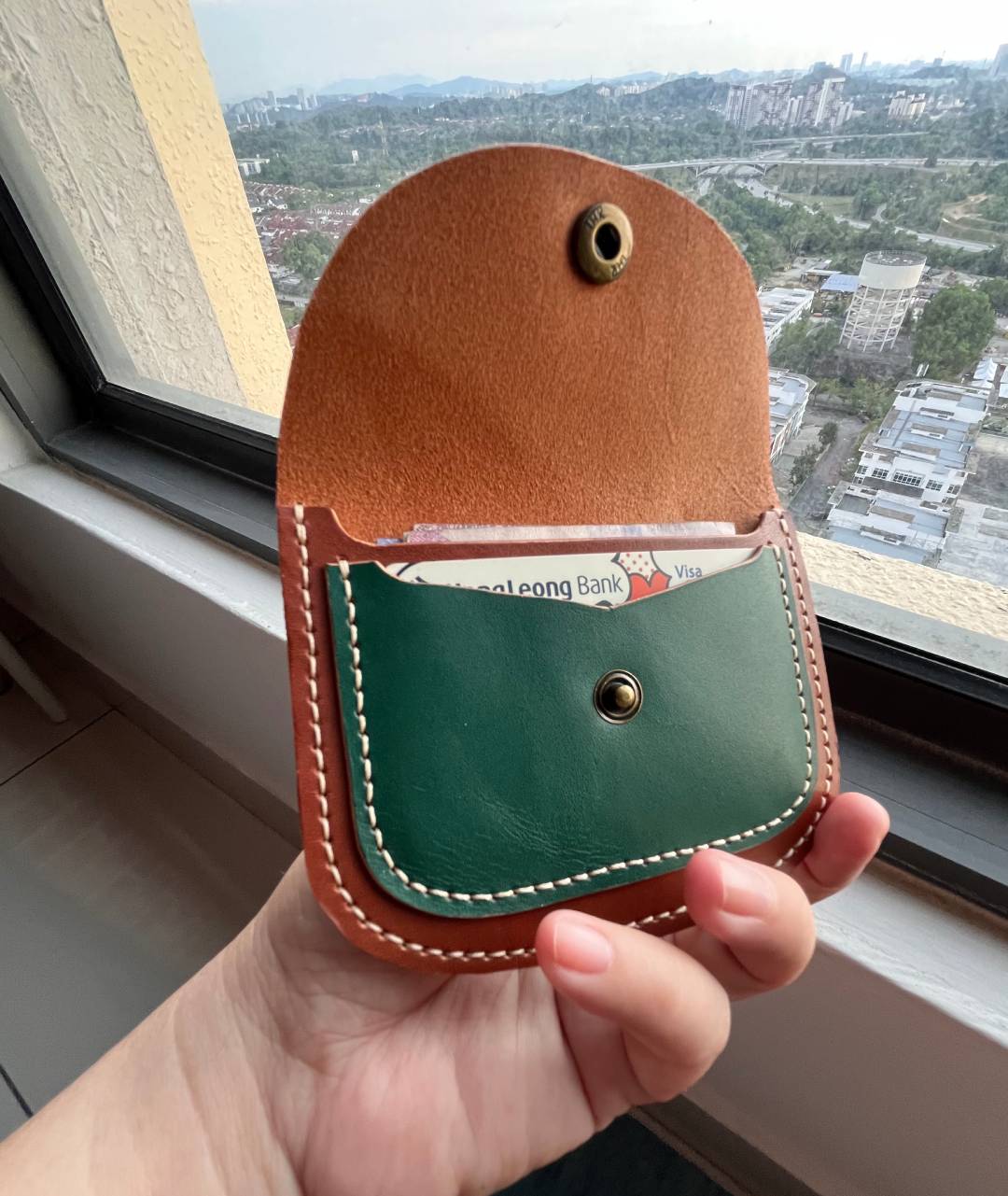 Hand holding the slim green leather wallet to show pocket-sized scale.