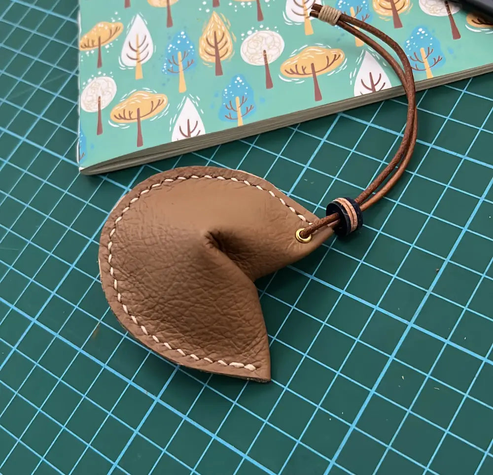 Leather fortune cookie attached to a designer brown leather handbag as a decorative charm.