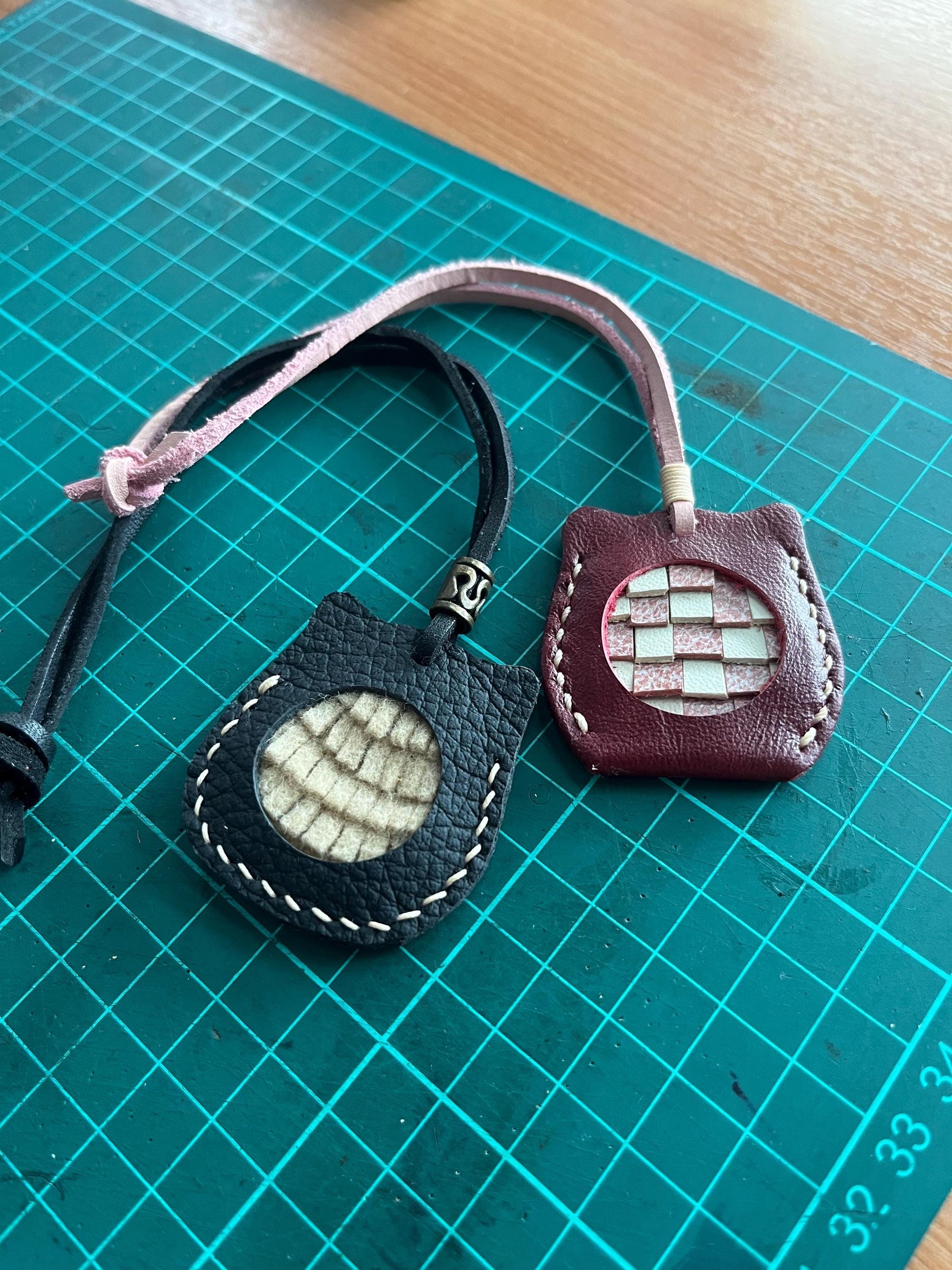 Two leather cat ornament with different patterns. One is black with a white and brown pattern, the other is burgundy with a white and pink checkered pattern.