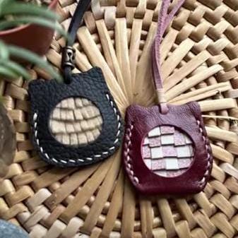 Two leather cat ornaments with a woven circle design. One leather cat ornament is black with a light brown woven circle, and the other is burgundy with a pink woven circle.