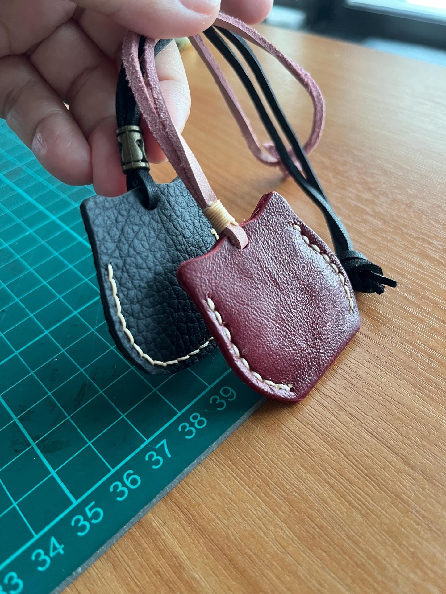 Back view of two leather cat ornaments. One is black with white stitching and the other is burgundy with white stitching.