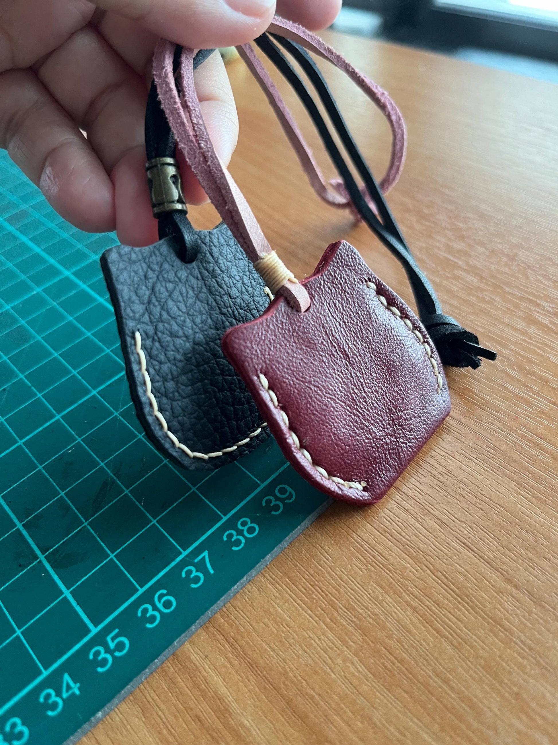 Back view of two leather cat ornaments. One is black with white stitching and the other is burgundy with white stitching.