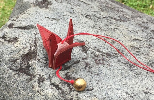 Red leather origami crane with a gold bell charm attached to a red cord.