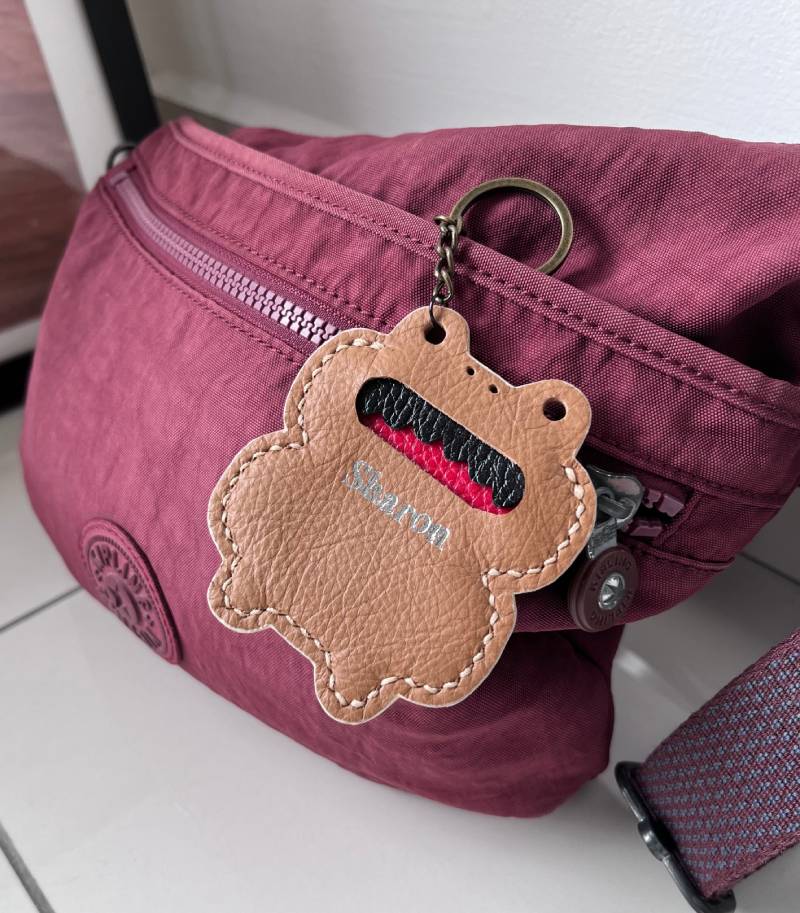A burgundy nylon fanny pack with a matching zip and a brown leather frog-shaped keyring.
