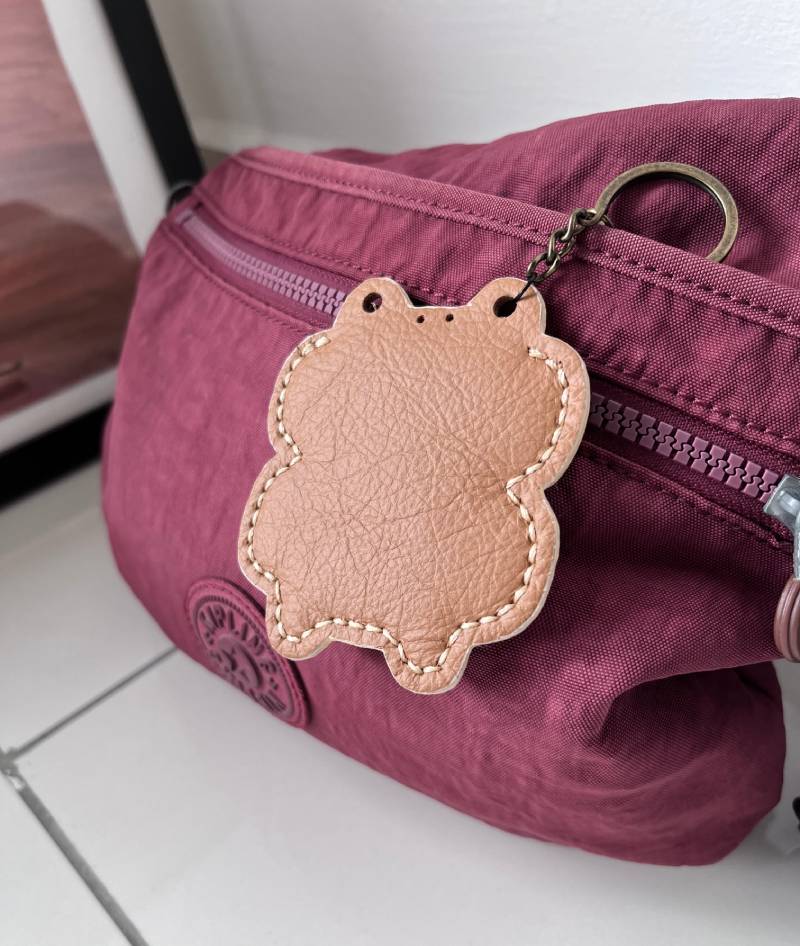 A burgundy nylon fanny pack with a matching zip and a brown leather frog-shaped keyring.
