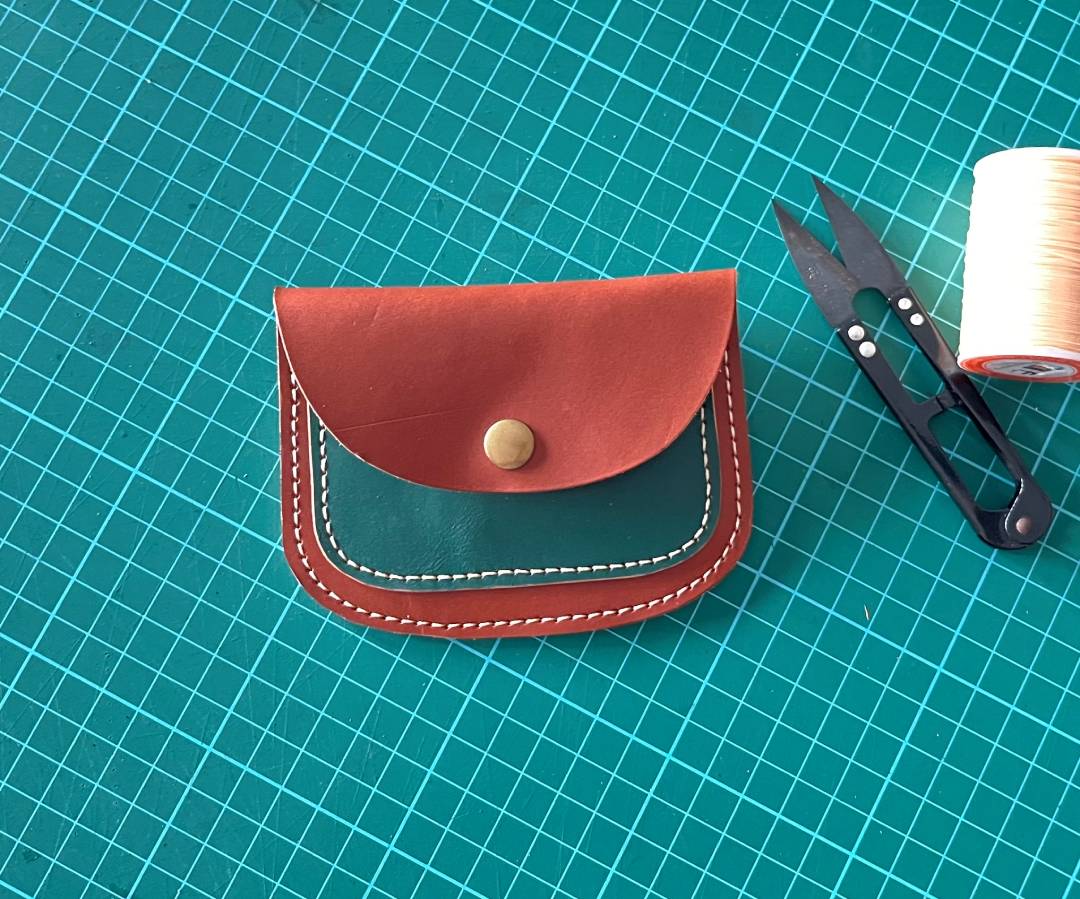 Front view of a green and tan minimalist leather card wallet with a snap closure.