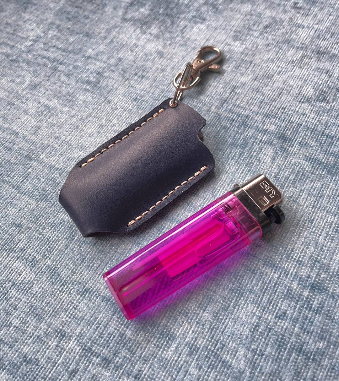 Pink lighter with a black DIY leather holder on a textured surface