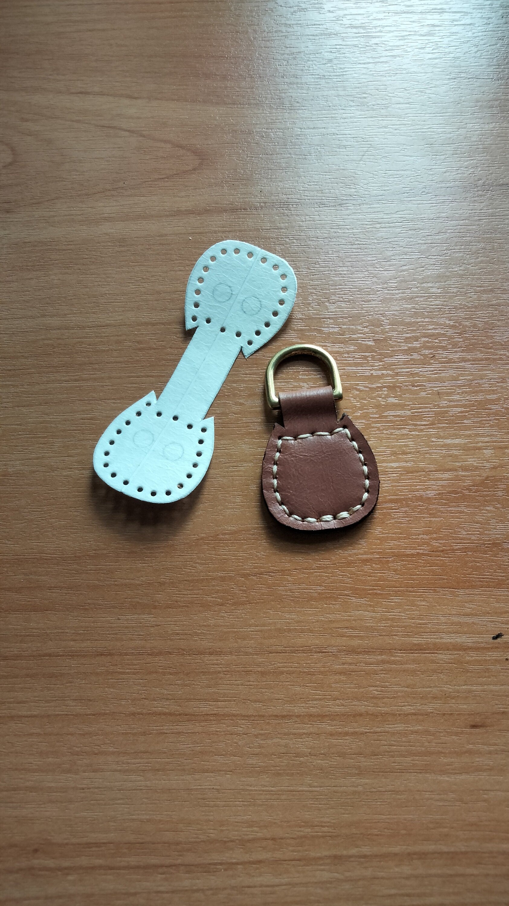 Light brown square leather keychain with white stitching on a brass ring, displayed with its leather pattern on the table.