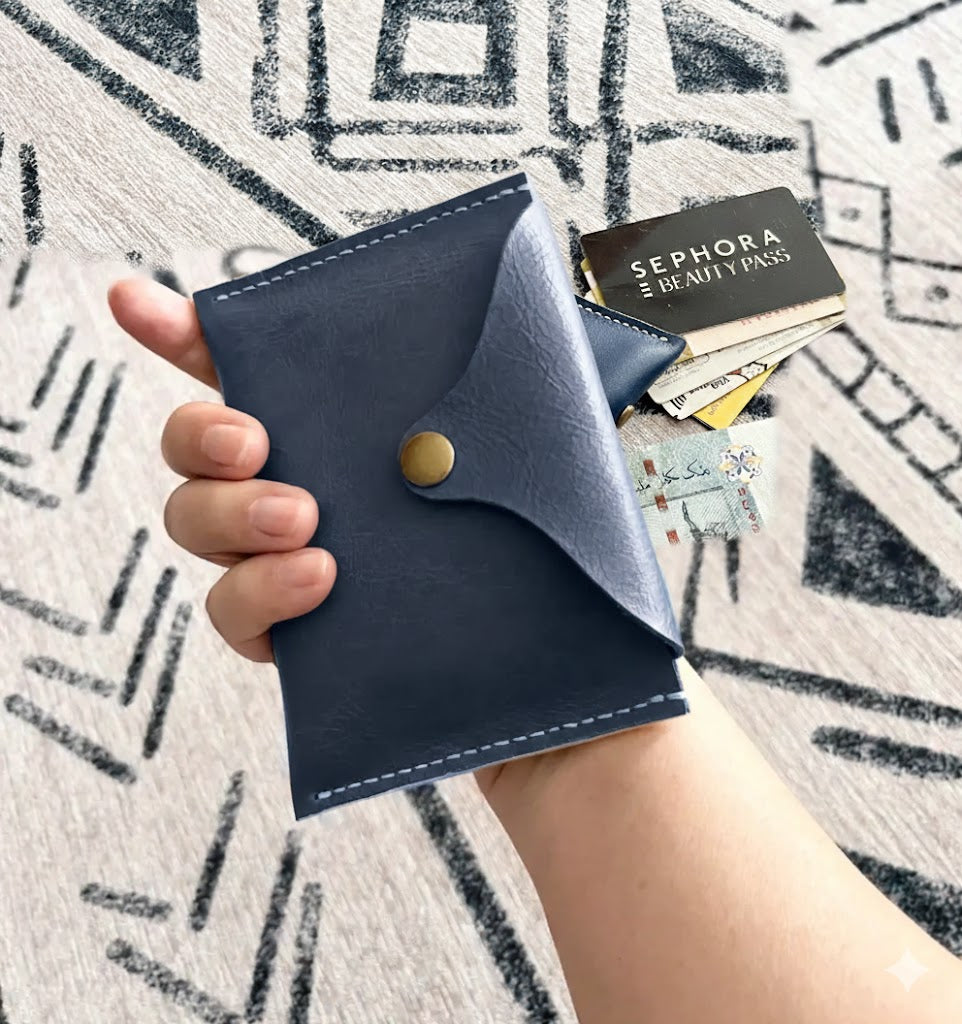 Close-up of a DIY navy leather card holder held in hand, showing textured leather and artisanal hand-stitched details.
