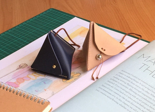 Two pyramid leather coin pouches. The pouches on the left is navy blue and the purse on the right is light brown.