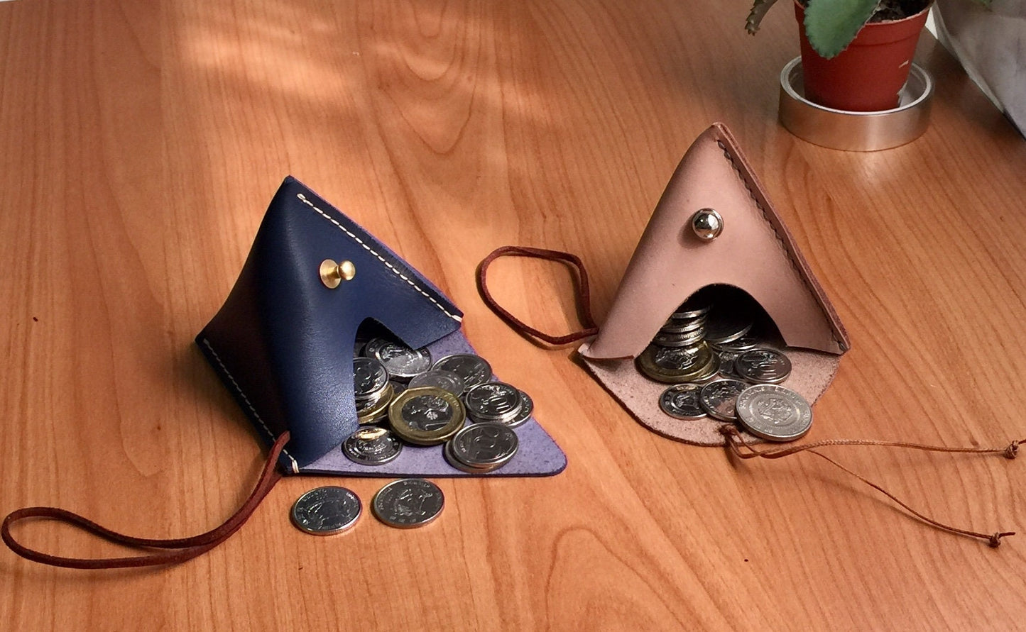 Two pyramid leather coin pouches. One pouch is blue with gold accents and the other is pink with silver accents. Both pouches are filled with coins.