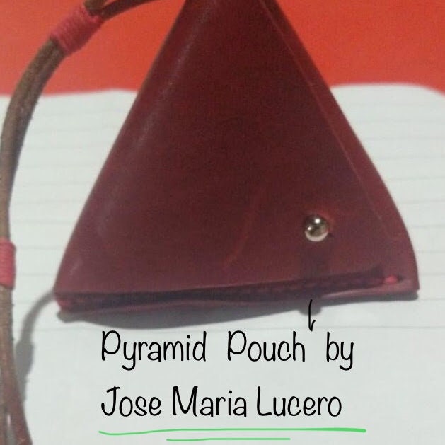 A red leather pyramid-shaped pouch with a silver button closure. The pouch has a brown leather strap.