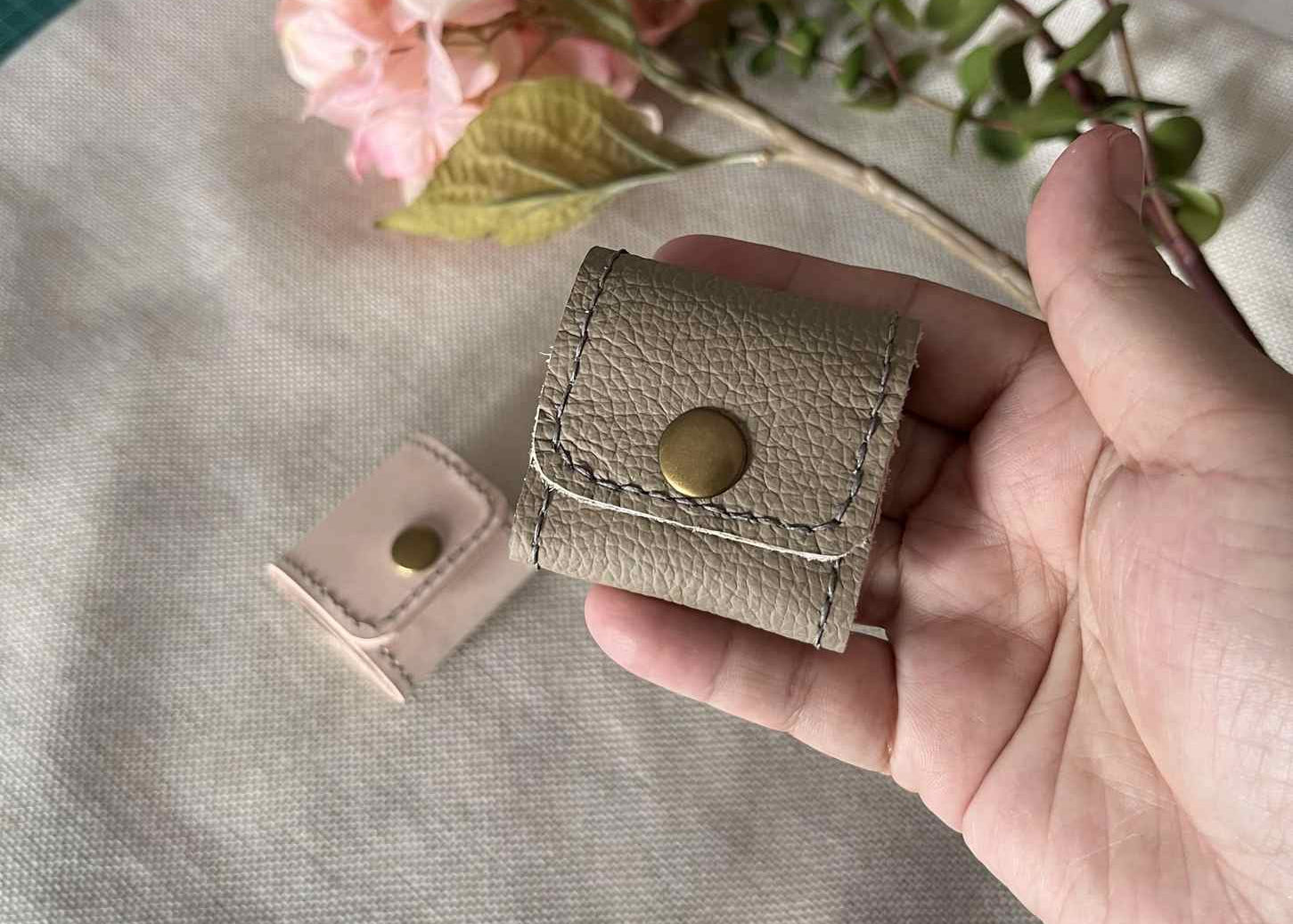 Folded tan leather mini accessory purse with a bronze snap closure on a textured background.