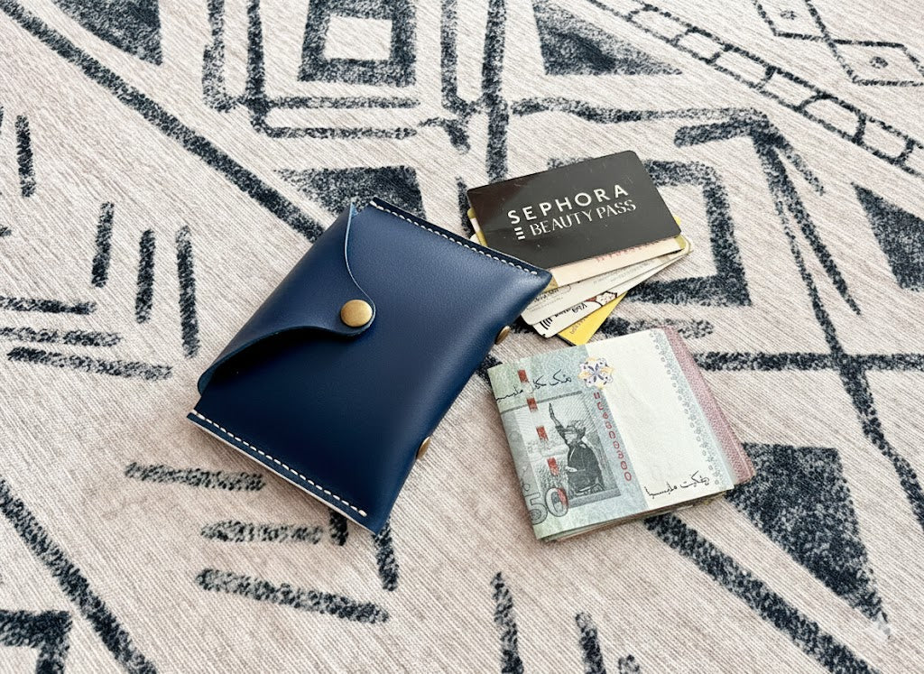 A slim, unisex blue leather pouch with a brass fastener, demonstrating the finished result of a beginner-friendly leathercraft project