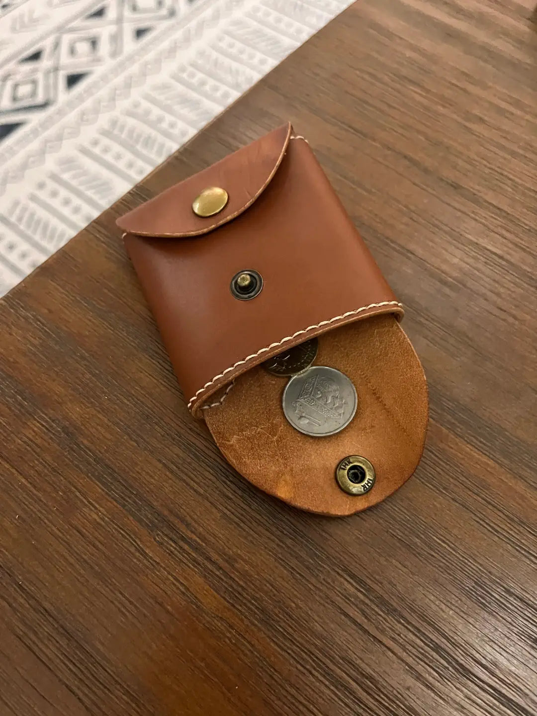 Small brown leather pouch with  few coins scattered on a wooden surface