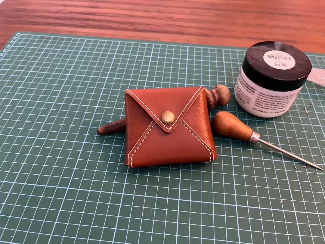 Brown square envelope leather coin pouch with tools on a grid surface