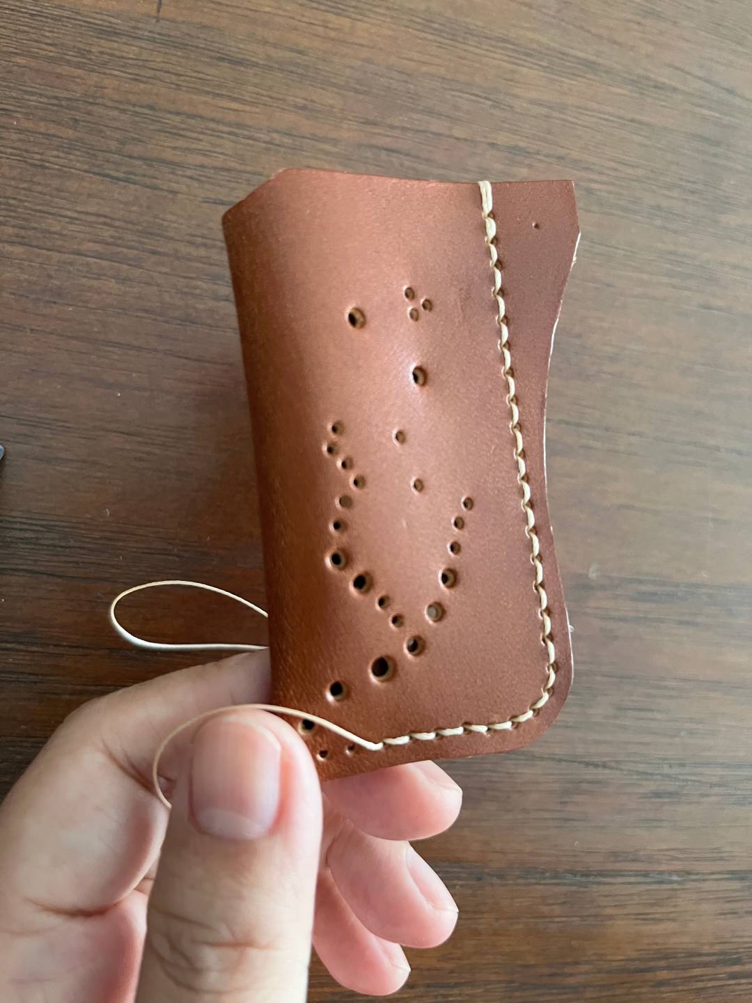 Brown leather lighter holder with hand stitching held by a hand on a wooden surface