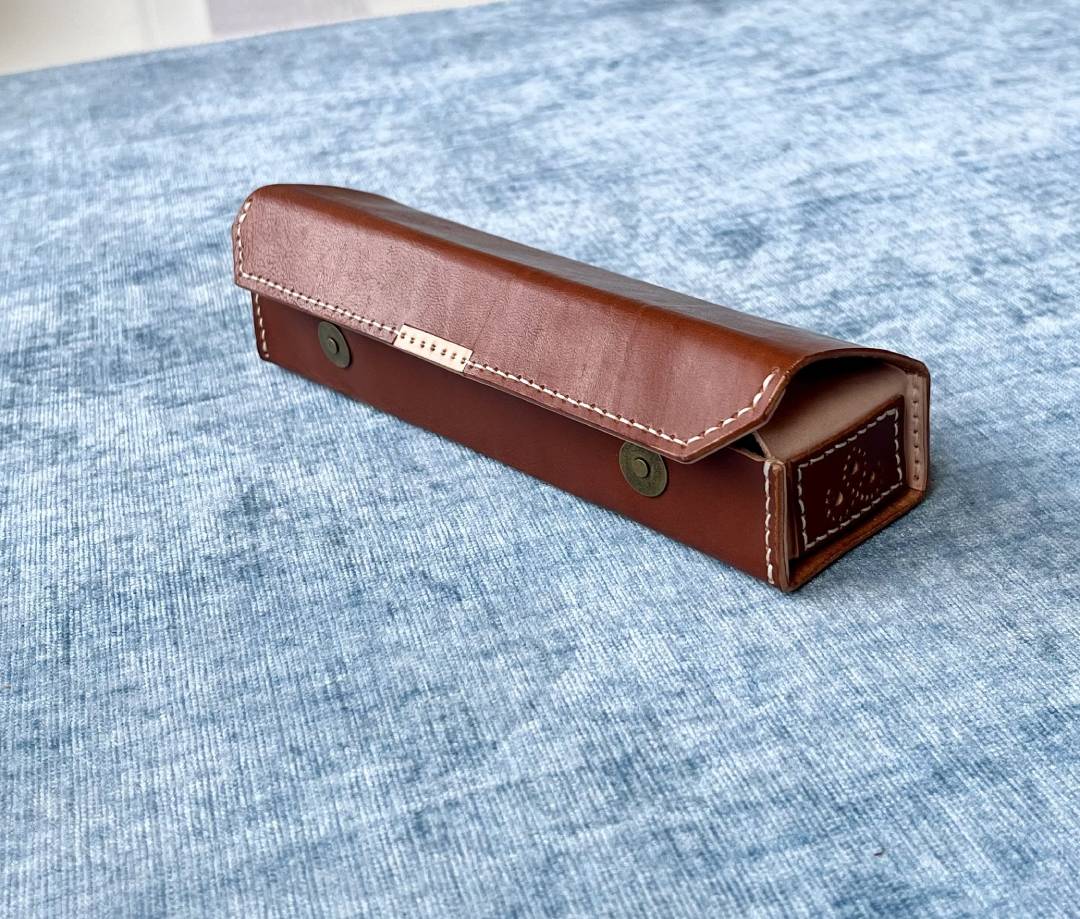 Leather pen case held in hand showing the textured brown finish and stitching.