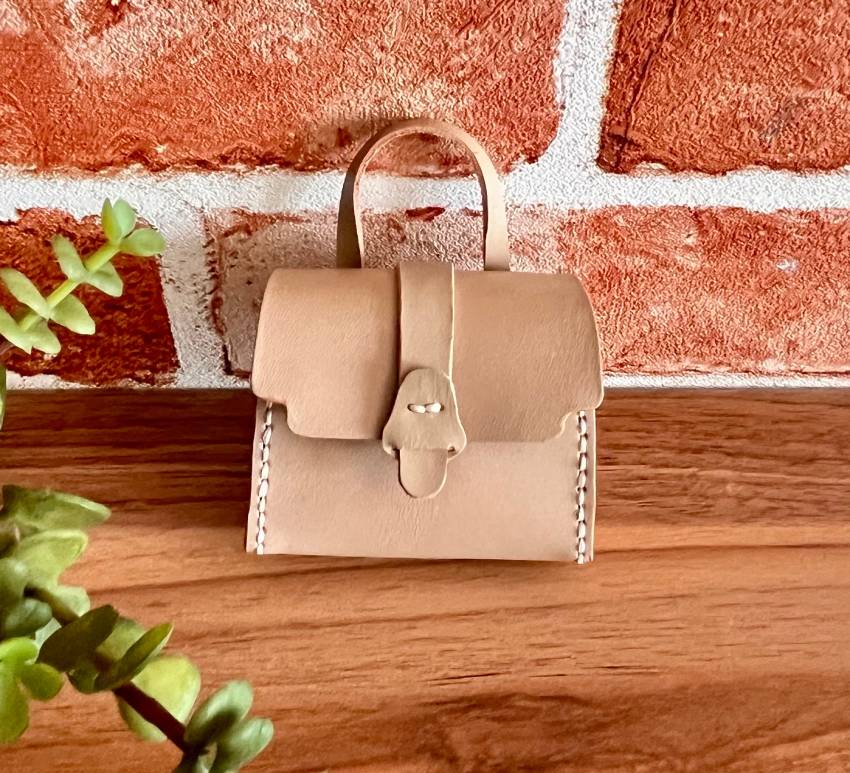 Front view of a tiny handmade leather  purse with a carry handle.