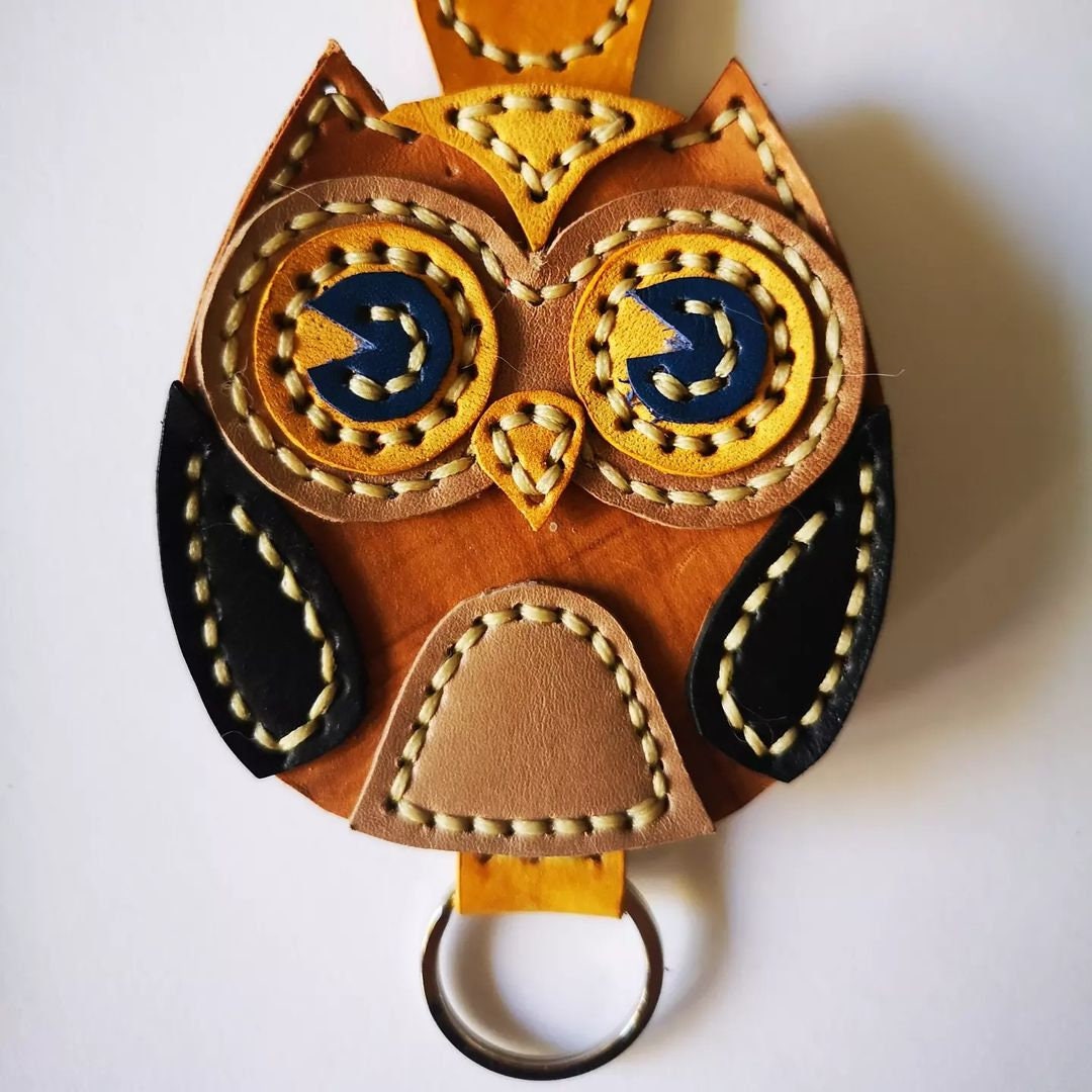 Red, blue, and tan leather owl charms with hand-sewn details and leather loops.