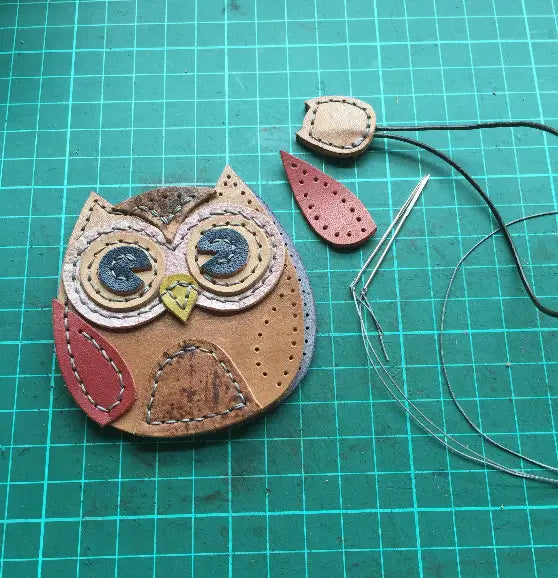 Multi-layered leather owl design featuring spiral-stitched eyes and teardrop wings.