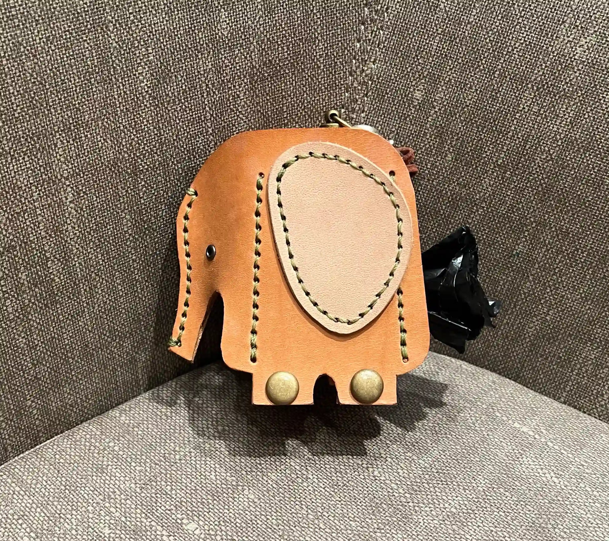 Elephant-shaped leather waste bag holder featuring green saddle stitching and brass snap hardware.