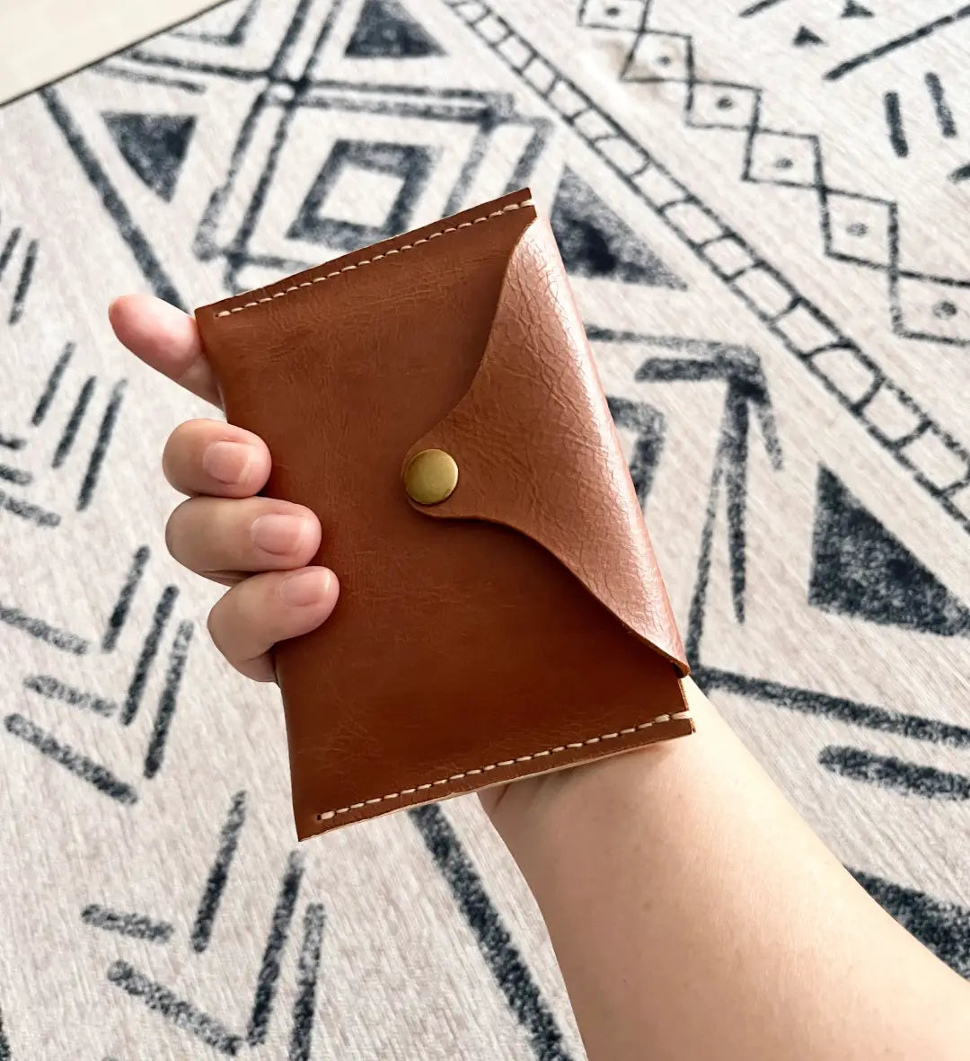 holding a handmade navy blue leather wallet with white saddle stitching and a brass snap button closure.