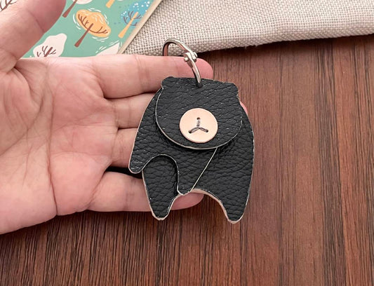 Black leather bear keyring with a button eye and a silver ring. The bear has a textured surface and a button for a nose. A cute accessory.