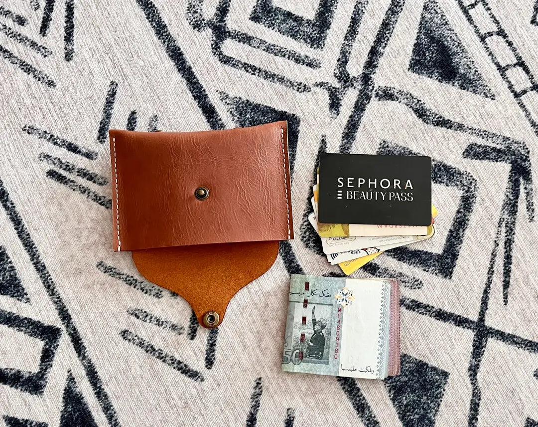 An open handmade tan leather wallet laying flat next to credit cards and folded banknotes.