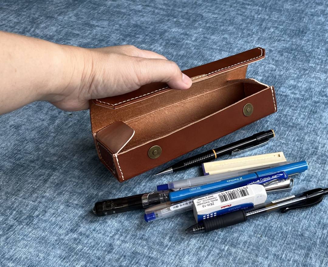 Open leather pencil box showing internal magnetic button clasps and pens.