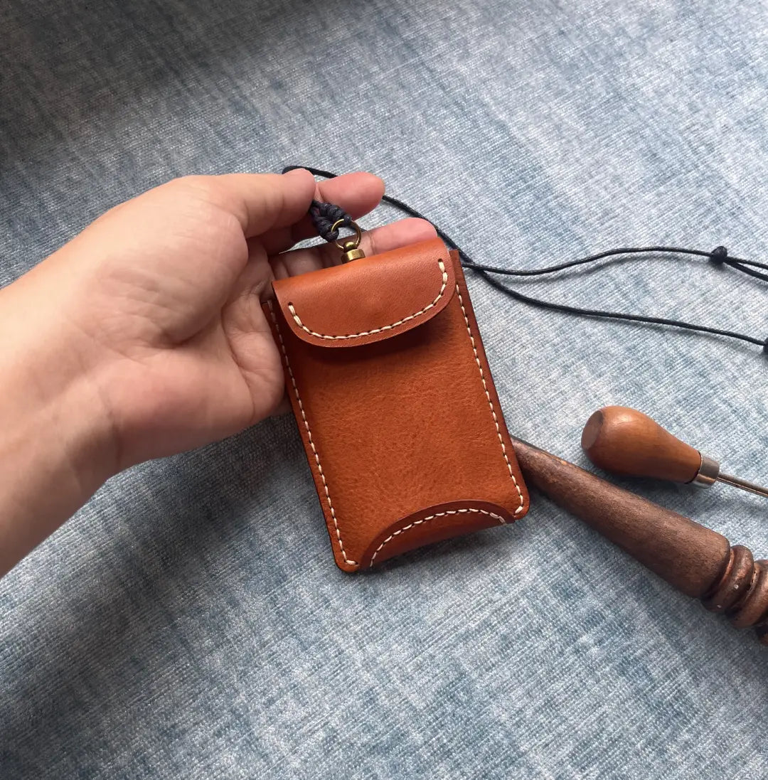 Hand holding a handmade leather card case to demonstrate its small, minimalist size and ergonomic curved pocket design.