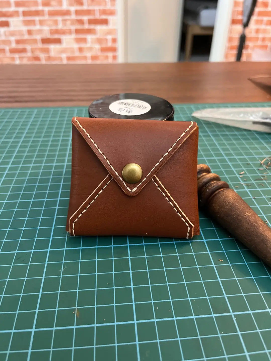 Brown leather coin pouch with a gold button on a green cutting mat.