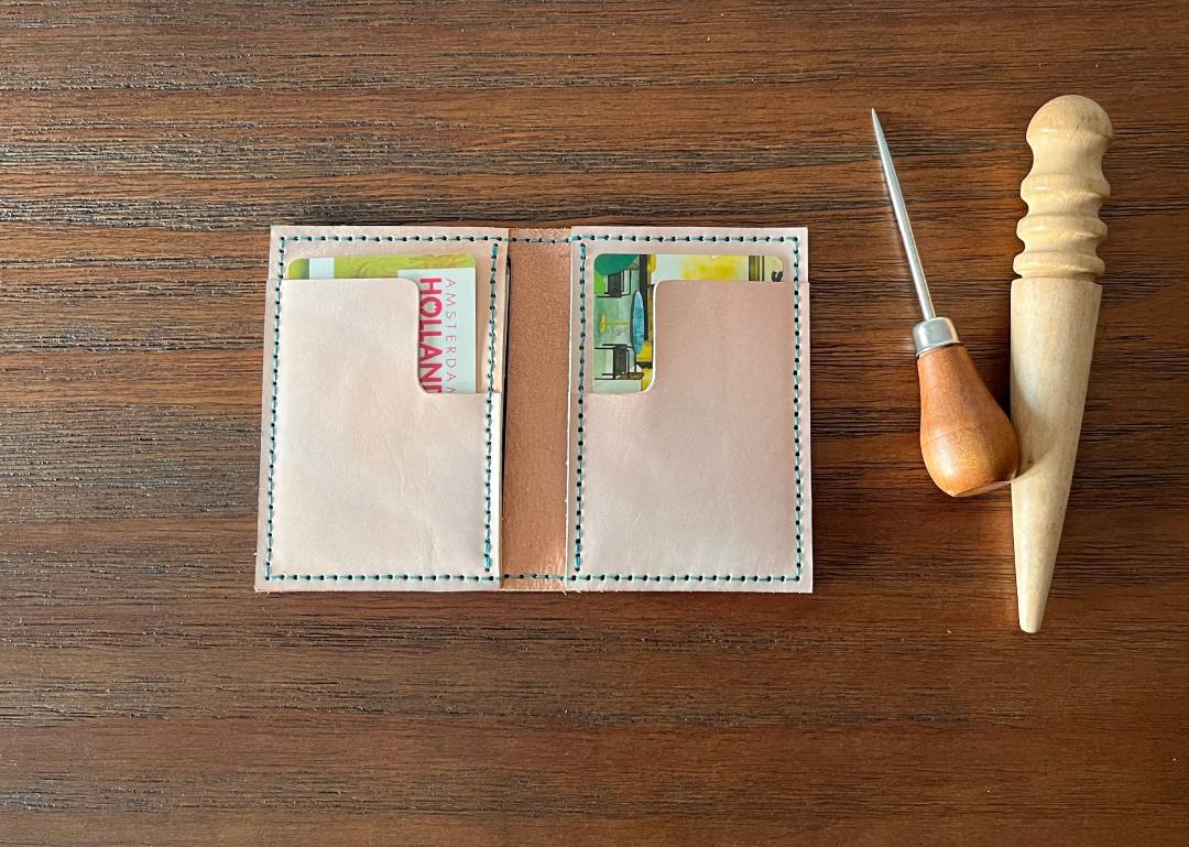 Front view of leather wallet holding cards on a wooden surface with a wooden tool.
