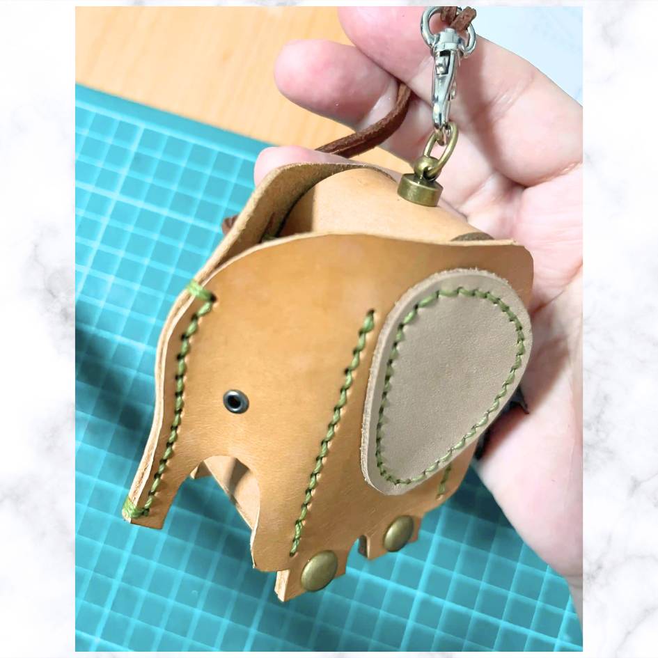 Premium leather elephant bag dispenser hanging from a gold-tone swivel clasp for dog walking.