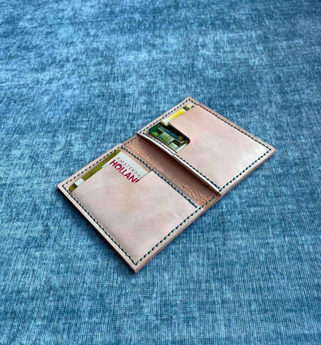Beige  minimalist leather card holder with card slots on a blue textured fabric background