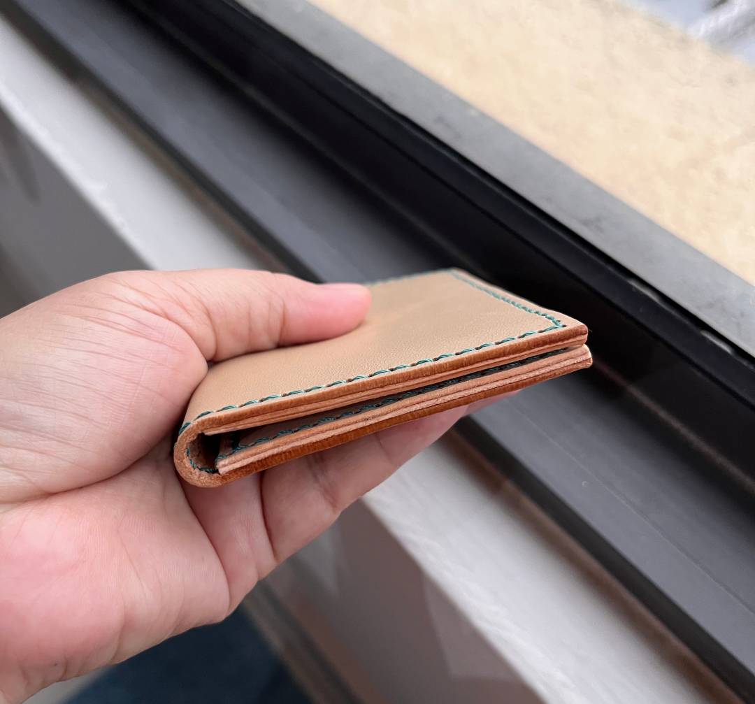Hand holding side view of a brown slim leather card holder wallet