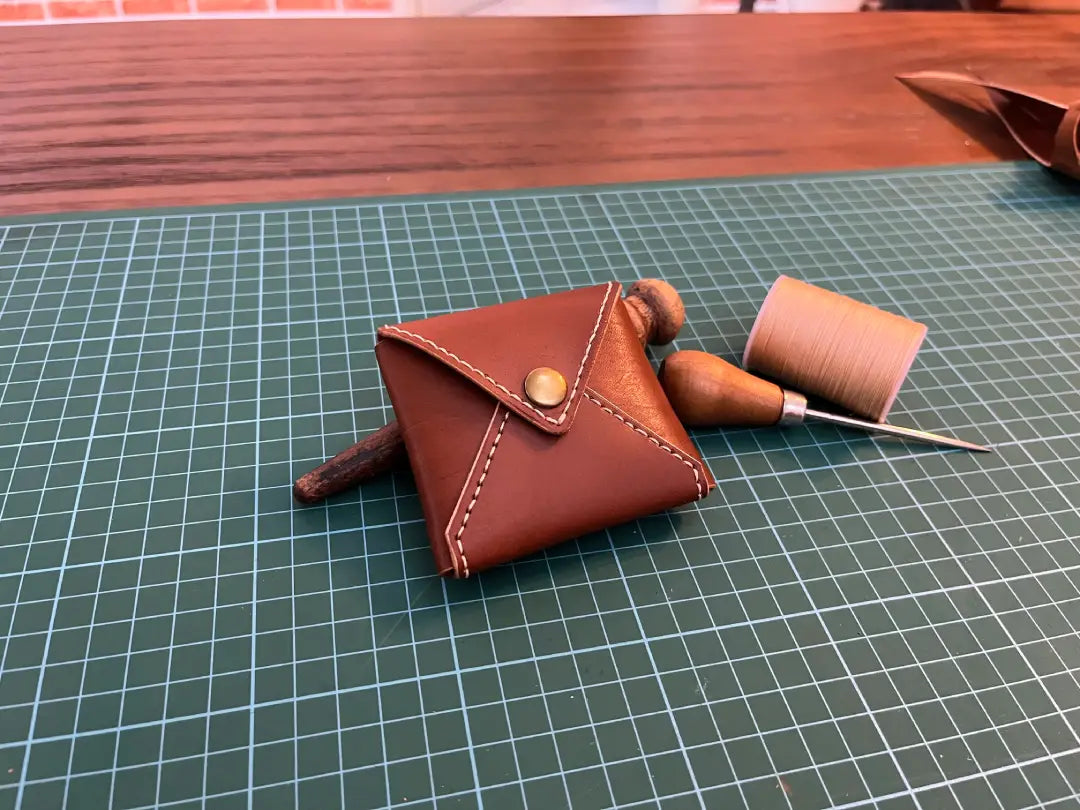 Small DIY brown leather coin  pouch with a button on a grid surface