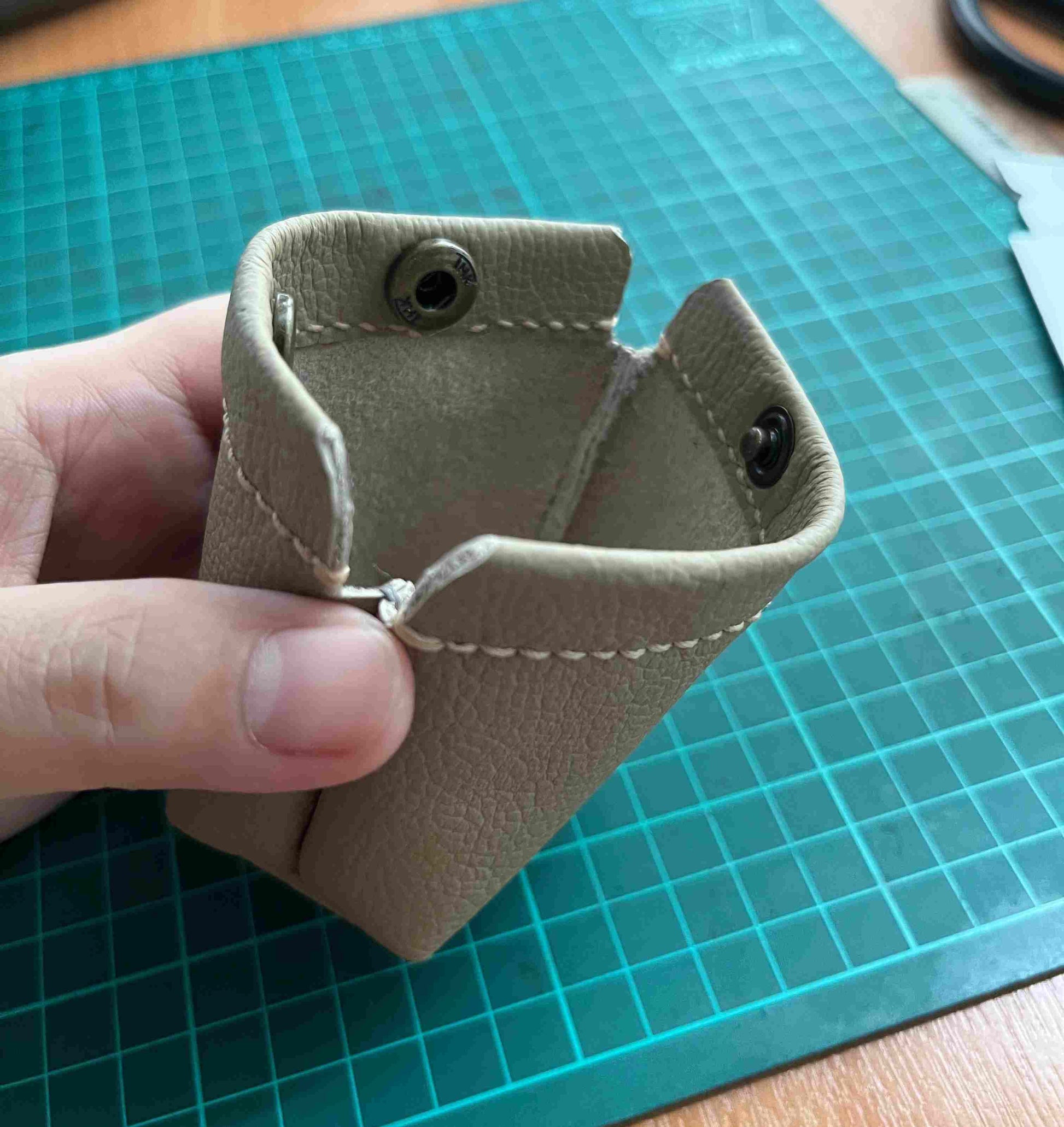 Minimalist small leather coin purse held between fingers to show compact scale.