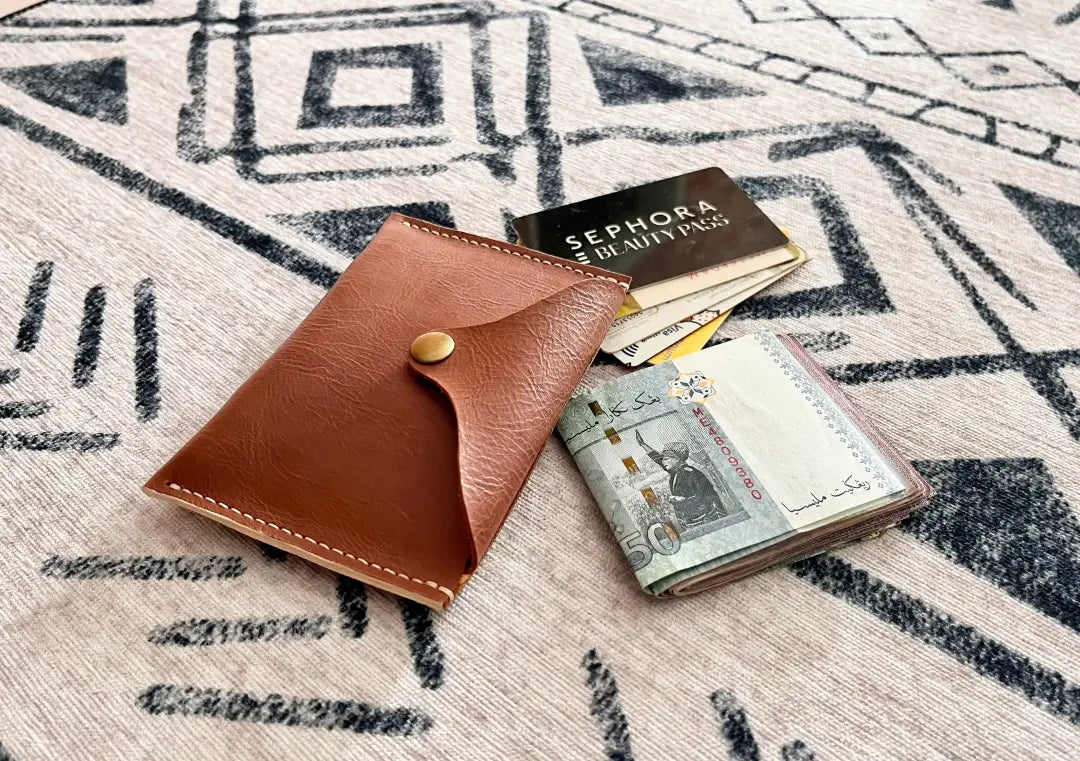 A versatile tan leather card and cash holder shown alongside everyday essentials, highlighting the utility of this DXF/SVG pattern design.