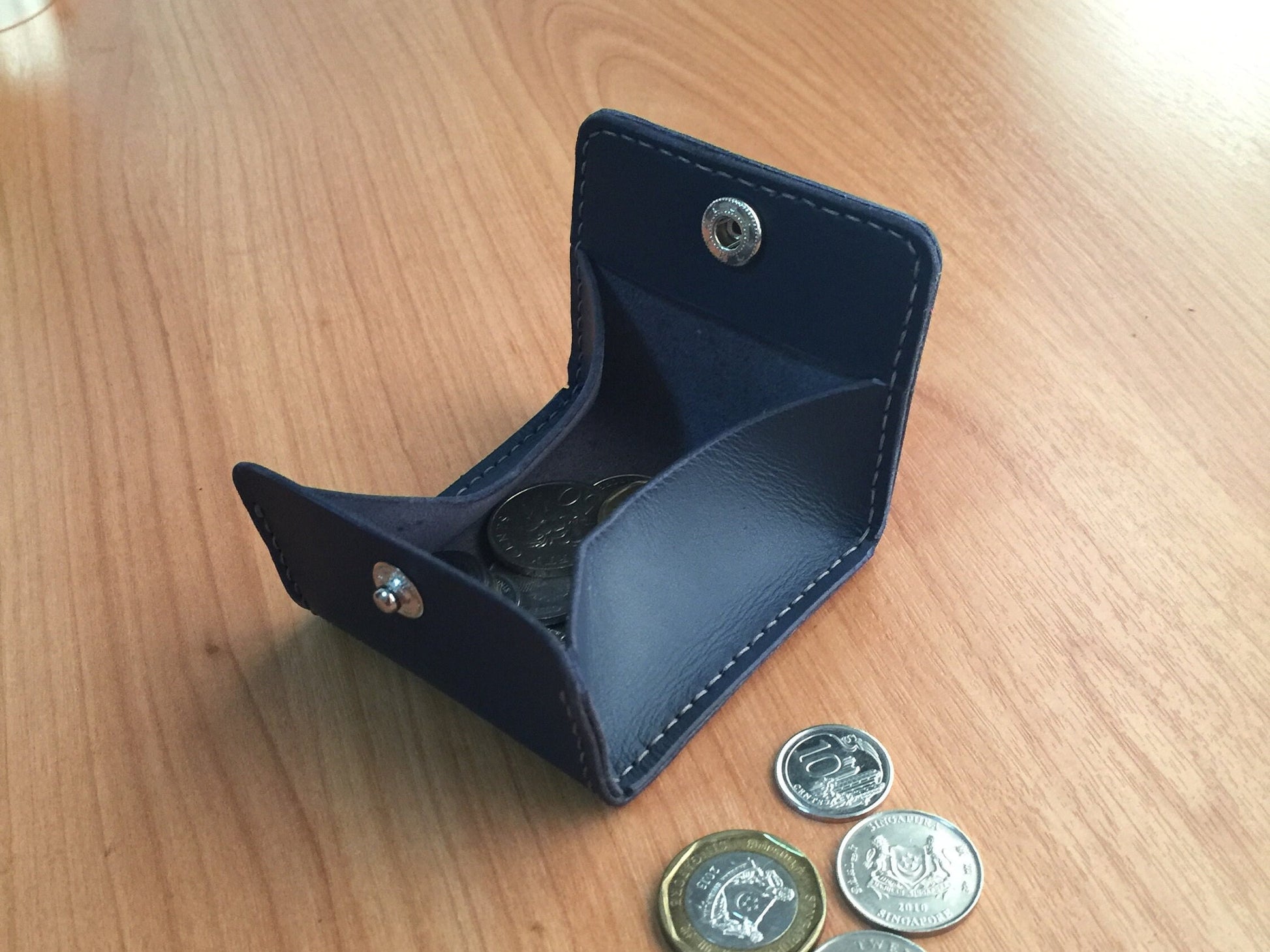 square leather pouch with a snap closure designed for coins and small accessories.