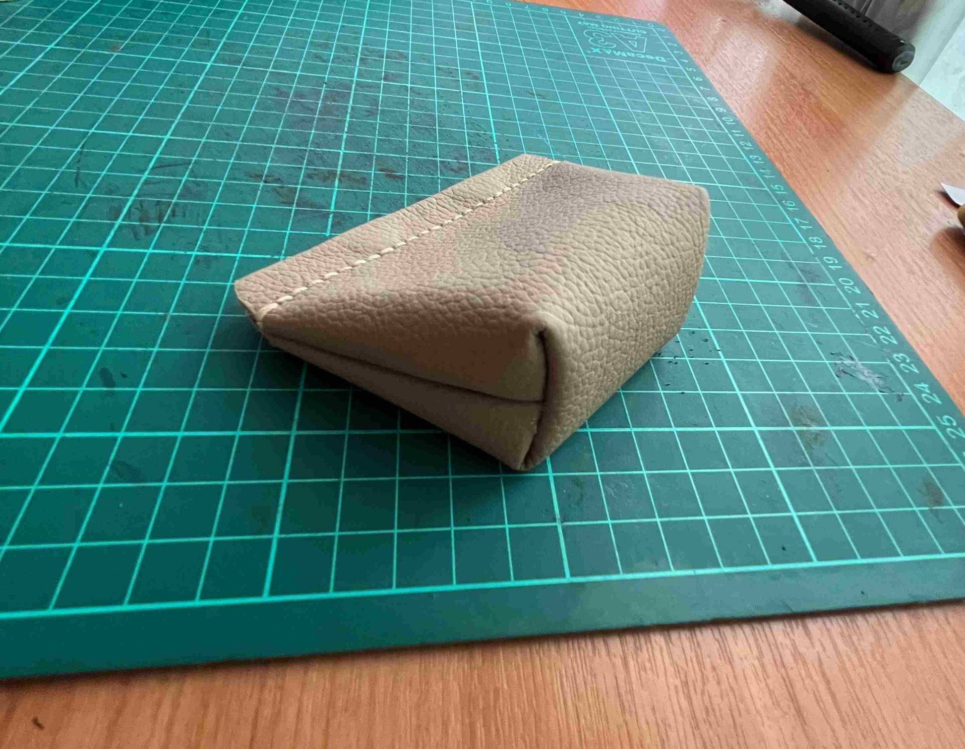 Close-up of a brass snap button closure on a tan leather coin pouch.