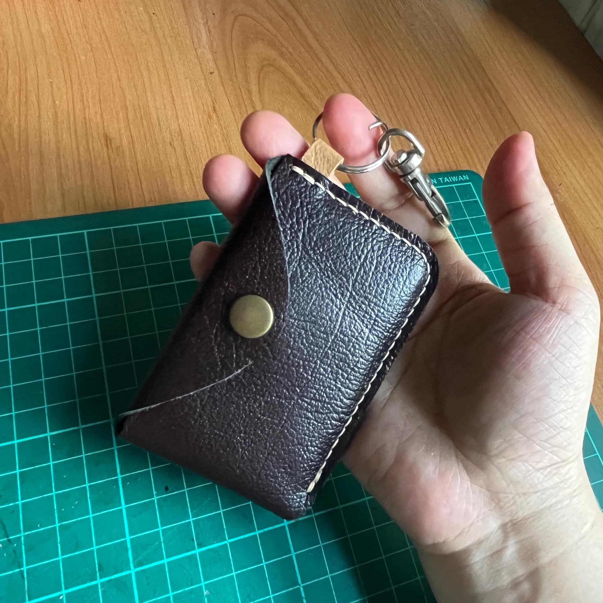 Leather card holder design with snapping button closure and single card slot.