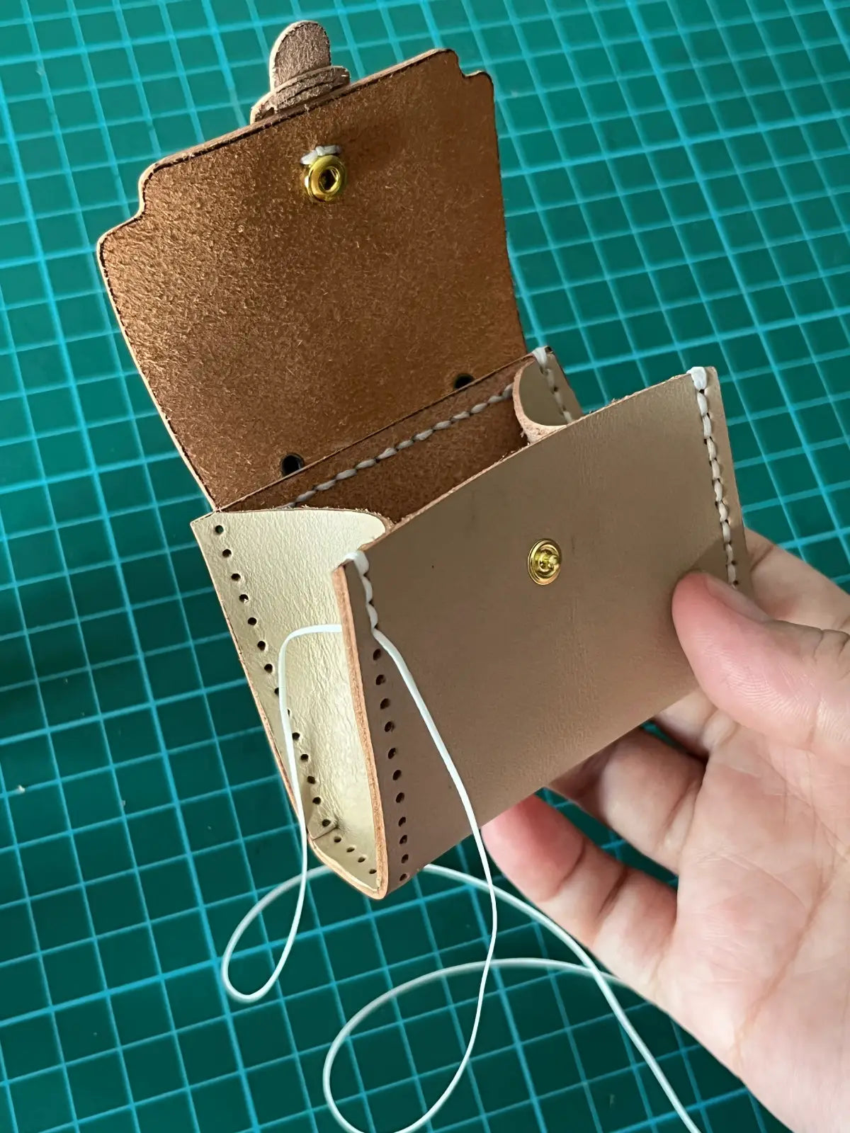 Stitching a tiny brown leather satchel bag with a hand holding it.