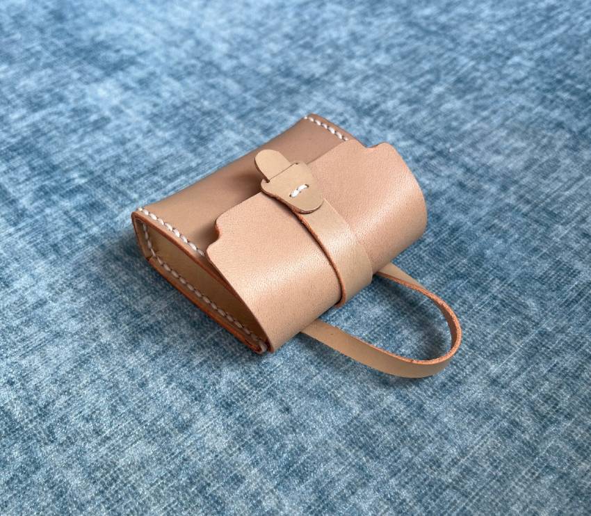 Tiny beige leather bag charm with a handle on a blue textured fabric background