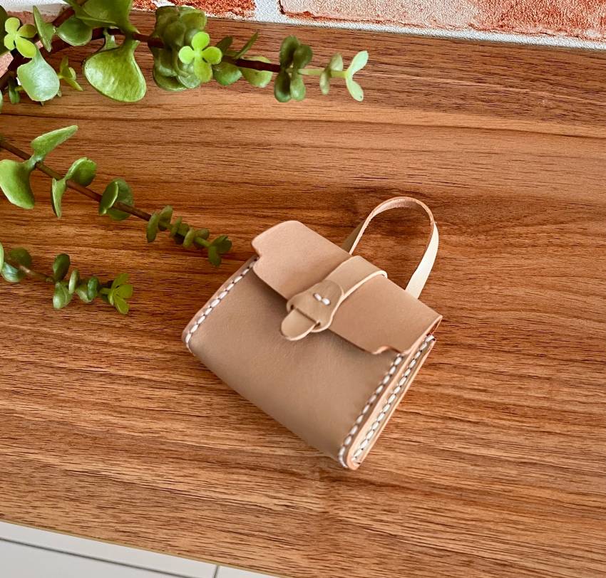 The finished tiny leather satchel laying on the wooden table