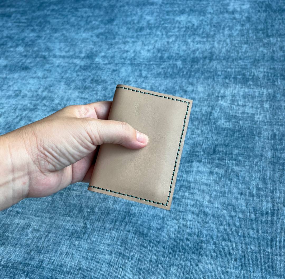 Hand holding a beige leather card wallet against a blue fabric background